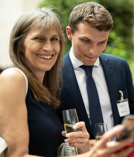 Woman smiling whilst holding her phone up whilst man staring at the screen